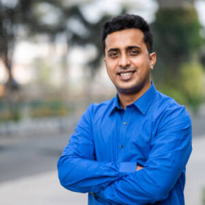 Outdoor Portrait of young Indian man with folded hands and looking at camera.